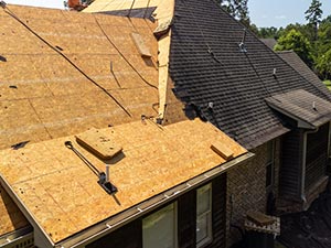 Residential roof under construction with exposed plywood sheathing and partially installed dark shingles; tools on the roof.