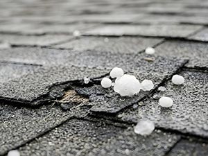Grey roof shingles with scattered white hailstones and a small damaged area nearby.