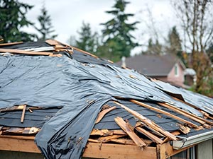 Storm-Damage-Missoula-MT-Montana-2 | Schrock Roofing Roof under repair with a black tarp and scattered wooden boards on a house roof in a residential setting.