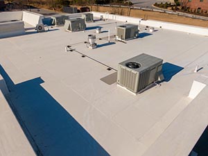 Rooftop scene with several packaged air conditioning units and vents on a white flat roof.